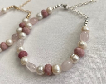 Puede incluir: Un delicado brazalete con una mezcla de cuentas rosas y blancas. El brazalete está hecho con una cadena de plata y un cierre de mosquetón.