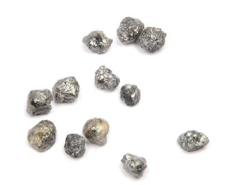May include: A collection of small, rough, black diamonds on a white background.