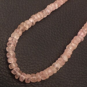 Puede incluir: Una hebra de cuentas de piedras preciosas de color rosa pálido, cada cuenta está facetada y tiene una forma ligeramente irregular. Las cuentas están enhebradas en un hilo transparente y están dispuestas en un diseño simple y elegante.