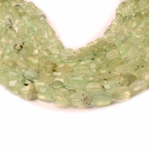 May include: A strand of light green gemstone beads, each bead is faceted and has a slightly irregular shape.
