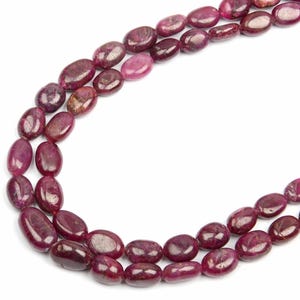 May include: A strand of oval-shaped ruby beads, with a deep red colour and a polished finish. The beads are strung on a clear thread and are arranged in a loose, flowing pattern.