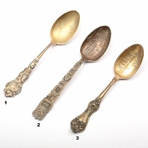 Puede incluir: Tres cucharas de plata con mangos ornamentados. Las cucharas están grabadas con diferentes diseños, incluyendo un edificio y un patrón floral.