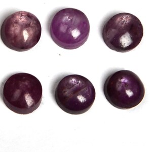 May include: Six round, purple gemstones with a smooth, polished finish. The gemstones are arranged in two rows of three.
