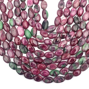 Pode incluir: Um fio de contas de pedras preciosas rosa e verdes. As contas são de forma oval e têm um acabamento liso e polido.