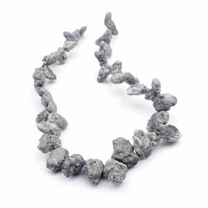 May include: A necklace composed of irregularly shaped, gray-colored beads. The beads have a rough, textured surface and are strung together on a thin, nearly invisible cord. The necklace is displayed against a white background.