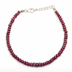 May include: A ruby bead bracelet with a silver clasp. The bracelet is made of small, round, deep red ruby beads strung together. The clasp is a silver lobster claw style with an adjustable chain.