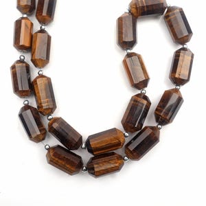 May include: A necklace featuring faceted, barrel-shaped beads in shades of brown and gold. The beads are strung together with silver-colored metal accents. The necklace is displayed against a white background.