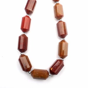 May include: A necklace featuring faceted, reddish-brown gemstone beads. The beads are strung together with small silver-colored connectors. The gemstones have a polished, glossy finish and a variety of shades.
