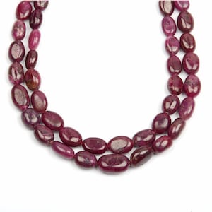 May include: A strand of deep red ruby gemstone beads, each bead is oval shaped and polished smooth. The beads are strung on a clear thread and are arranged in a double strand.
