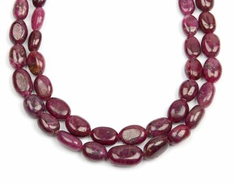 May include: A strand of deep red ruby gemstone beads, each bead is oval shaped and polished smooth. The beads are strung on a clear thread and are arranged in a double strand.