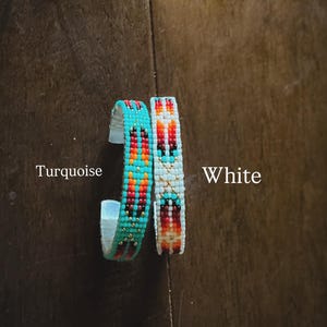 May include: Two beaded bracelets, one turquoise and one white, with a Native American-inspired design. The turquoise bracelet has red, orange, and gold accents. The white bracelet has red, orange, and gold accents. The word "Turquoise" and "White" are visible.
