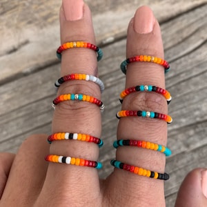 May include: A set of colourful beaded rings with a variety of patterns. The rings are made with small, colourful beads and feature a mix of orange, red, white, black, and turquoise beads.