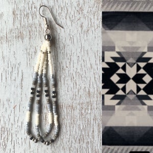 May include: A pair of long, beaded earrings with a silver hook. The earrings are made with white, gray, and black beads.