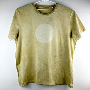 May include: A short-sleeved, olive green t-shirt with a large, faded white circle design on the front. The shirt is hanging on a white hanger against a white background. The fabric appears soft and slightly worn.