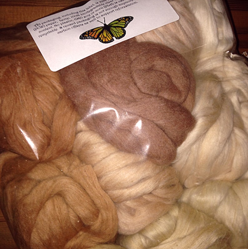 Op de afbeelding: Een doorzichtige plastic zak met meerdere bundels ongesponnen wolvlies in verschillende tinten bruin, beige en cr&egrave;me. Aan de bovenkant zit een wit rechthoekig label met een afbeelding van een monarchvlinder en gedrukte tekst over de verpakking.