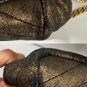 May include: Close-up of a small, quilted handbag with a metallic gold and black finish. The bag features a gold chain strap. The texture of the bag is visible, showing a sparkling, glittery effect.