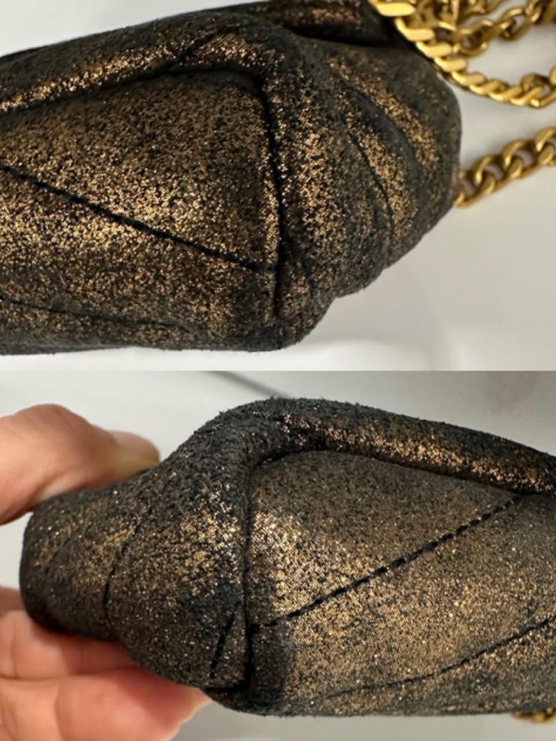 May include: Close-up of a small, quilted handbag with a metallic gold and black finish. The bag features a gold chain strap. The texture of the bag is visible, showing a sparkling, glittery effect.
