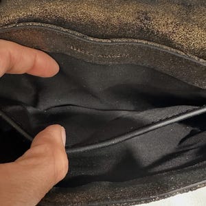 May include: Close-up of a black and gold metallic handbag interior. The bag's interior is black, with a visible pocket and a textured, shimmering exterior. The bag appears to be made of leather or a similar material.