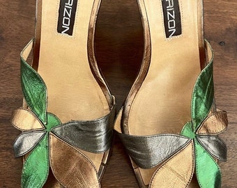 May include: A pair of gold and silver metallic heeled sandals with green leather flower accents. The sandals are made in Italy by Maud Frizon Paris.