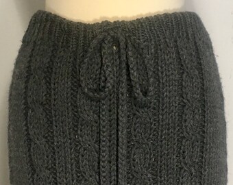 May include: A gray knitted skirt with a cable knit pattern and a tassel tie at the waist.