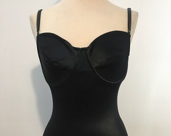 May include: A black bodysuit with a sweetheart neckline and adjustable straps. The one-piece garment has a fitted silhouette and is displayed on a mannequin. The fabric appears to have a slight sheen.