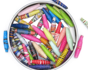 May include: A tin container filled with colorful paper beads. The beads are made of rolled up paper and are in a variety of colors, including pink, blue, green, yellow, and red.