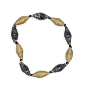 May include: A handmade necklace featuring alternating black and gold-colored paper beads. The beads are strung together with black string and small gold-colored beads. The necklace is displayed against a white background.