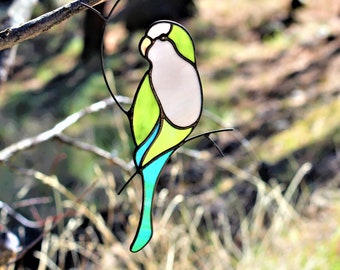 May include: A stained glass bird with green, blue, and white glass pieces. The bird is perched on a branch.