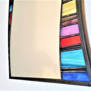 May include: A curved mirror with a stained glass frame. The frame features a series of colorful glass panels in shades of blue, red, yellow, and pink.