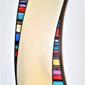 May include: A curved mirror with a black frame and a colorful stained glass border. The border features a variety of colors, including blue, red, yellow, and purple.