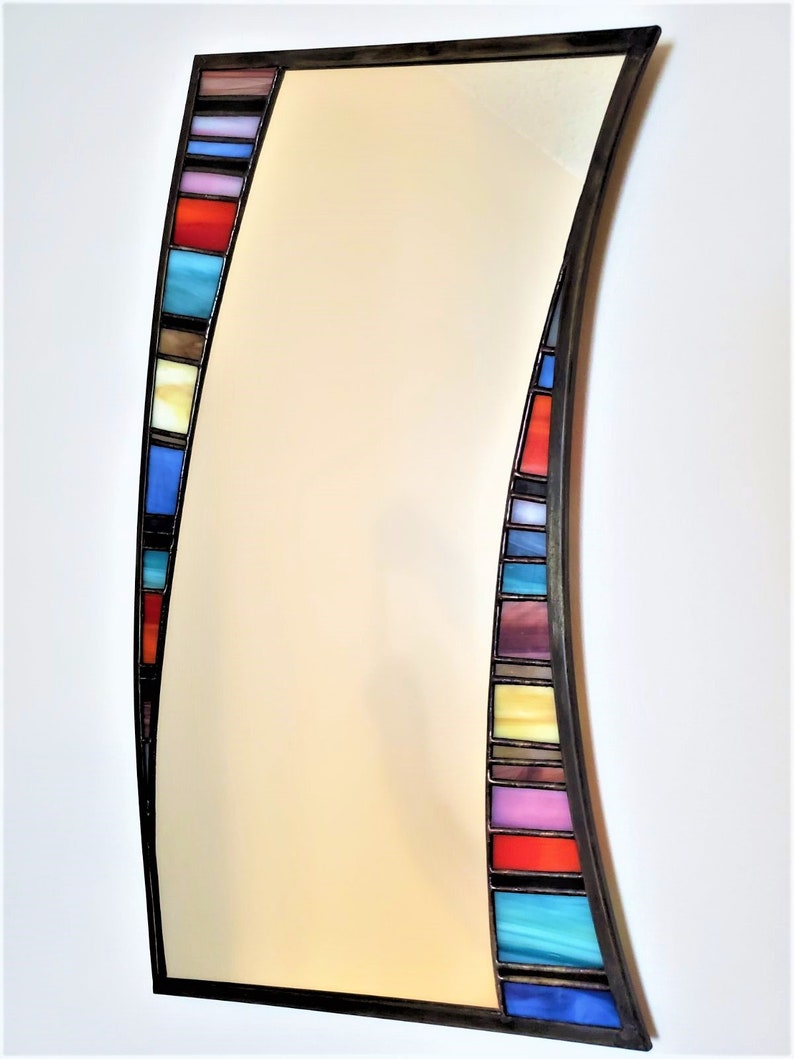May include: A curved mirror with a black frame and a colorful stained glass border. The border features a variety of colors, including blue, red, yellow, and purple.