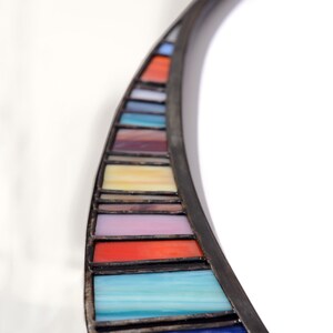 May include: A curved mirror with a black frame and a colorful stained glass border. The border features a rainbow of colors, including red, orange, yellow, green, blue, indigo, and violet.