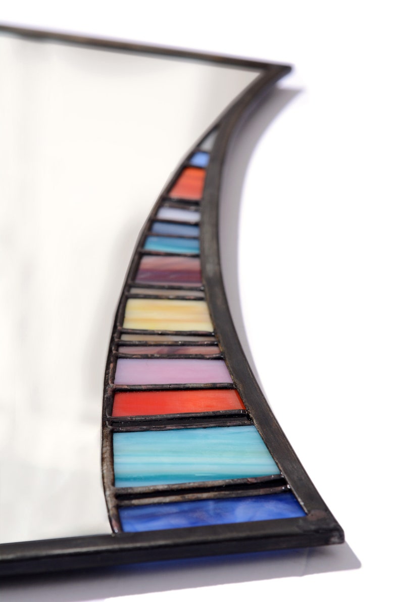 May include: A curved mirror with a black frame and a colorful stained glass border. The border features a rainbow of colors, including red, orange, yellow, green, blue, indigo, and violet.