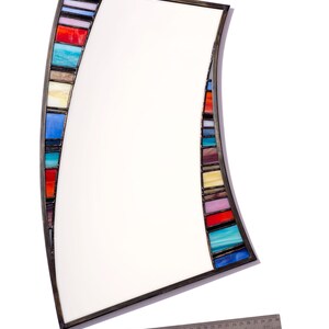 May include: A curved mirror with a metal frame and a colorful mosaic border. The mosaic is made of small, rectangular pieces of glass in various shades of blue, red, yellow, and green.