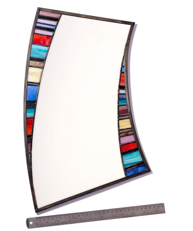 May include: A curved mirror with a metal frame and a colorful mosaic border. The mosaic is made of small, rectangular pieces of glass in various shades of blue, red, yellow, and green.