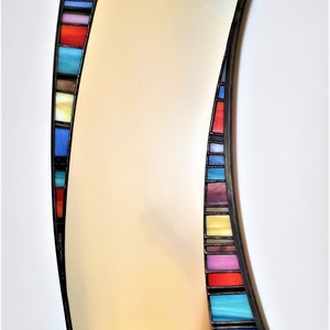 May include: A curved mirror with a black frame and a colorful stained glass border. The border features a variety of colors, including red, blue, green, yellow, and purple.