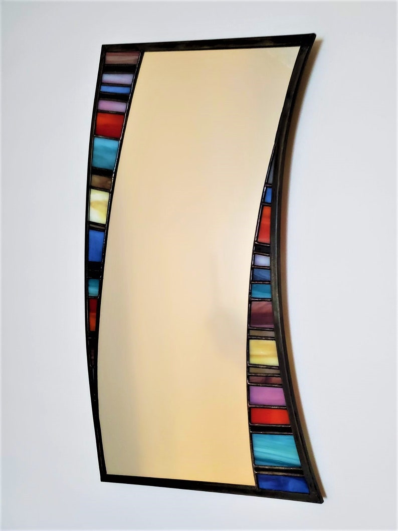 May include: A curved, rectangular mirror with a black frame and a colorful stained glass border. The border features a variety of colors, including blue, red, yellow, and purple.