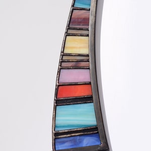 May include: A curved mirror with a stained glass frame. The frame is made of black metal and features a rainbow of colors, including blue, green, yellow, orange, red, and purple.