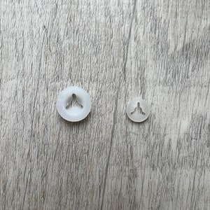 May include: Two white plastic snap fasteners, one larger than the other, on a woodgrain surface.