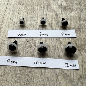 May include: Six pairs of black plastic safety eyes for crafts, ranging in size from 5mm to 12mm. The eyes are on a white surface with labels indicating the size of each pair.