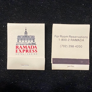 May include: Two matchbooks on a black surface. One features the Ramada Express Hotel Casino logo in red and grey. The other has the text "For Room Reservations" and a phone number.