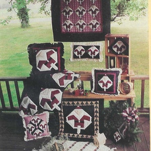 Pode incluir: Uma coleção de almofadas e tapeçarias acolchoadas feitas à mão com um design de floco de neve vermelho e branco. As colchas são exibidas em uma varanda de madeira com um gramado verde ao fundo.
