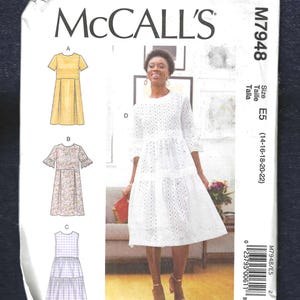 May include: McCall's sewing pattern M7948 for a dress in sizes E5 (14-16-18-20-22). The pattern includes three different styles: a yellow dress with a gathered skirt, a floral print dress with short sleeves and ruffles, and a white eyelet dress with a tiered skirt.