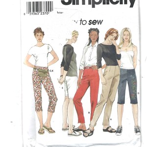 Op de afbeelding: Een Simplicity naaipatroon envelop 9064, maat A 6-16, met illustraties van diverse kledingstijlen waaronder een wit t-shirt, een bloemrijke capribroek, een top met raglanmouwen, een witte korte broek, een overhemd, een rode broek en een zwarte top.