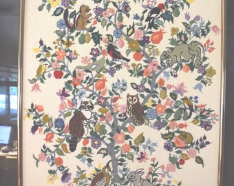 May include: A framed cross-stitch embroidery depicting a tree filled with colourful flowers, fruits, and various animals including a raccoon, an owl, a rabbit, a chipmunk, and several birds. The artwork features the initials CW and the year 83.