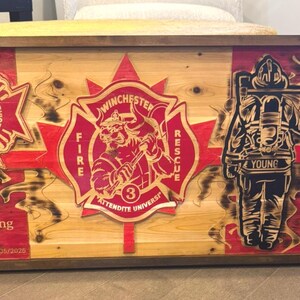 Peut inclure: Plaque en bois avec un motif de drapeau canadien, des emblèmes de pompiers et une silhouette de pompier. La plaque comprend le texte "Richard Young #306" et des dates. L'œuvre est dans les tons rouge, noir et bois naturel.