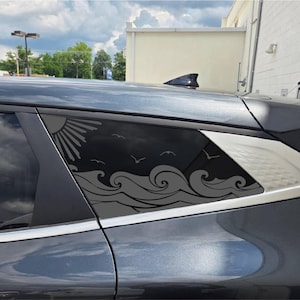 May include: A dark gray car window decal featuring a stylized ocean scene with rolling waves, a sunburst in the upper corner, and several birds flying across the sky. The graphic is applied to the rear side window of a dark gray vehicle.