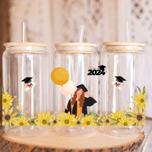 May include: Three clear glass tumblers with bamboo lids and straws. Each tumbler features a graduation theme with a yellow sunflower design, a graduation cap, a diploma, and the text "Class of 2024".