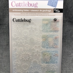 May include: A clear plastic embossing folder with a snowflake design. The folder is labelled "Cuttlebug" and "Provo Craft".