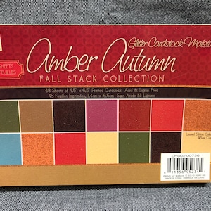May include: A pack of 48 sheets of 4.5 by 6.5 inch glitter cardstock in autumn colors. The pack is labeled "Amber Autumn Fall Stack Collection" and features a variety of colors including green, brown, red, orange, and yellow. The cardstock is acid and lignin free.